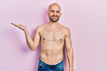 Canvas Print - Young bald man standing shirtless smiling cheerful presenting and pointing with palm of hand looking at the camera.