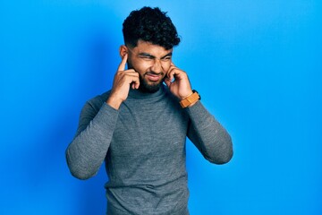 Poster - Arab man with beard wearing turtleneck sweater covering ears with fingers with annoyed expression for the noise of loud music. deaf concept.