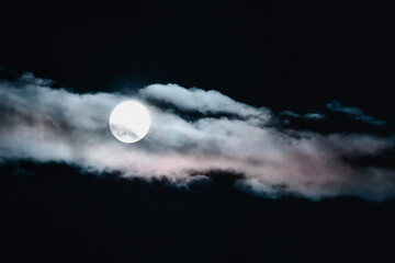 blurry unfocused full moon in the night sky hidden behind clouds tinted with sunset light