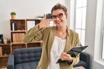 Poster - Young woman working at consultation office pointing with hand finger to face and nose, smiling cheerful. beauty concept