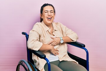 Poster - Young hispanic woman sitting on wheelchair smiling and laughing hard out loud because funny crazy joke with hands on body.