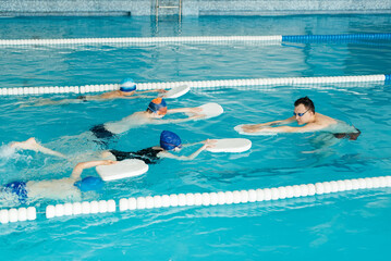 Wall Mural - A group of boys and girls train and learn to swim in a modern swimming pool with an instructor. Development of children's sports. Healthy parenting and promotion of children's sports.