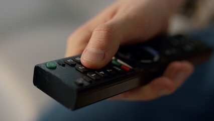 Fingers pushing remote control buttons closeup. Unknown man switching channels.