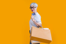 Asian Happy Senior Female Woman Tattoo Holds Colourful Shopping Packages Standing On Yellow Background Studio Shot, Close Up Portrait Old Female Hand Hold Shopping Bags Enjoy Shopping With Joyful