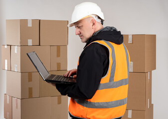 Poster - Warehouse manager. Man with laptop in front of boxes. Warehouse manager in protective hard hat. Human with computer is processing orders. Work on warehouse fulfillment. Guy in front cardboard parcels