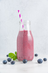 Wall Mural - Fresh blueberry smoothie in a glass bottle with straw and mint on white background. Summer refreshing drink