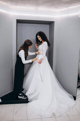 Wall Mural - Female making adjustment to wedding gown in fashion designer studio. Bride wearing her wedding gown with female dress designer making final adjustments on dress.