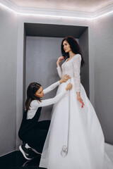 Wall Mural - dressmaker helping the bride to put her wedding dress on in clothes shop.