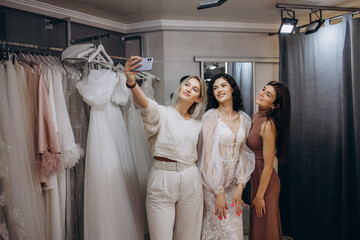 Wall Mural - Beautiful bride is trying on an elegant wedding dress in modern wedding salon, her friends are helping