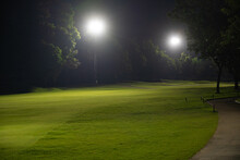 Beautiful Dark Night View Of The Golf Course, Bunkers Sand And Green Grass, Garden Background In The Light Of The Spotlight Underexposure View. Film Camera Look Photo Noise And Grain.