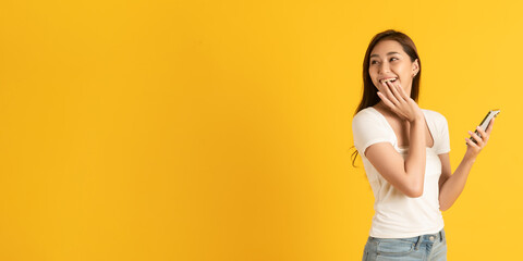 Wall Mural - Surprise happy asian beautiful woman isolate on yellow background using smartphone look at blank copy space area