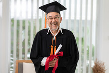 Asian Elderly In Cap And Gown Smile And Celebration Proud Success Graduate. Cheerful Senior Man Holding Certificated Or Diploma Glad And Happiness. Elderly Graduation Concept