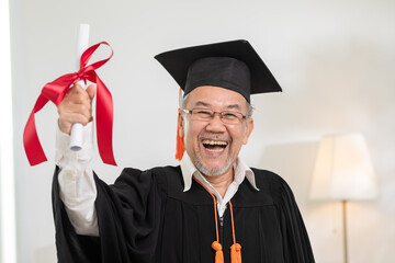 Asian elderly in cap and gown smile and celebration proud success graduate. Cheerful senior man holding certificated or diploma glad and happiness. Elderly graduation concept