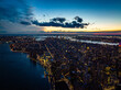 Breath taking aerial panoramic evening shot of city surrounded by river. Lighted windows and colourful sunset sky. Manhattan, New York City, USA