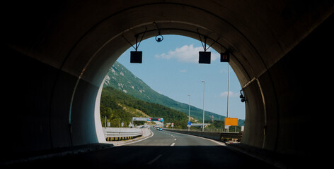 Photo of driving through a dark tunnel on a mountain highway with a view of the light at the end of the tunnel.