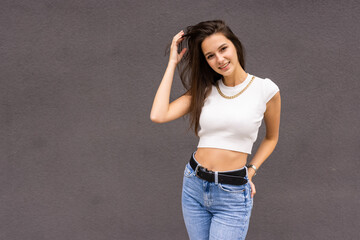 Young woman wearing blank white t-shirt and denim shorts posing against gray street wall, blank mockup for tshirt print store