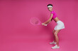 Beautiful young woman holding tennis racket while standing against pink background