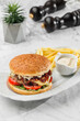 Tasty burger with french fries and sauce at the white plate on light marble background. Healthy sea food, hard light, restaurant decor, close up