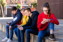 Teen Male And Female Students Sitting Together Outdoor Ignoring Each Other While Browsing Internet On Smartphones