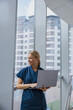 Smiling female healthcare worker using laptop while working at doctor's office and looking window