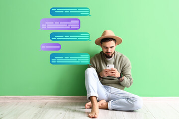 Handsome man with mobile phone chatting online near green wall