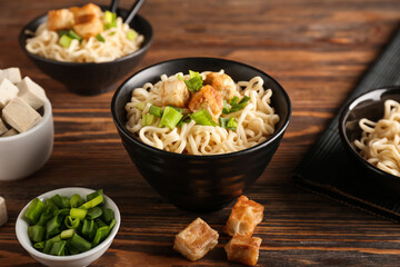 Bowls of tasty noodles with chicken on wooden background