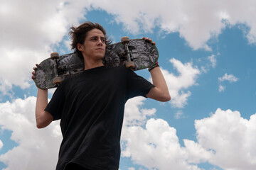 young guy in a black t-shirt posing with his skateboard on his shoulders