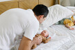 © Westend61 - Smiling man playing with baby on bed at home