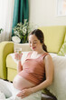 © Westend61 - Smiling woman with glass of water sitting by sofa at home