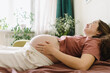 © Westend61 - Smiling pregnant woman lying on sofa bed at home