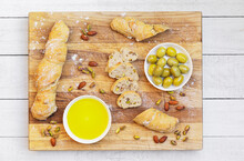 Studio shot of bowl of olive oil, green olives and loaves of homemade Pain Paillasse bread with almonds and pistachios