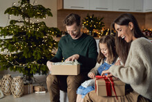 Happy Parents With Daughter Opening Christmas Present In Living Room