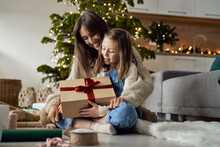 Girl Holding Christmas Present Sitting With Mother On Floor At Home