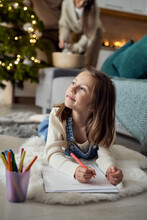 Thoughtful Girl Writing Letter To Santa Claus With Parents In Background At Home