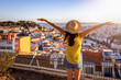 Leinwandbild Motiv A happy tourist woman overlooks the colorful old town Alfama of Lisbon city, Portugal, and castle Sao Jorge during golden sunset time