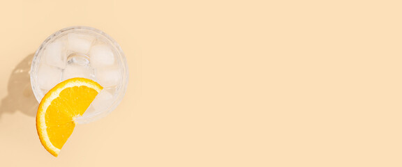 Glass with a cocktail with an orange slice on a beige background. Top view, flat lay. Banner