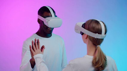 Poster - Multiethnic couple play virtual reality simulation in goggles isolated over neon background.