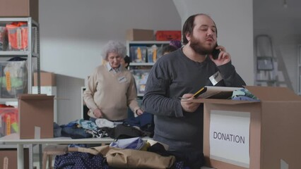 Wall Mural - Overweight man with clipboard talk on phone working in volunteering center