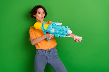 Poster - Photo of astonished positive person arms hold pump water weapon look empty space isolated on green color background