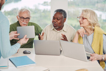 A small group of multicultural senior students in a classroom are looking at tablet with explanation and using laptops.