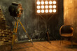 © Infusorian - Studio video photo movie equipment in the room in loft style. Old vintage light source on tripod stand, light panel with many light bulbs and a chair in a grunge interior, stylish photozone. High