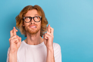 Wall Mural - Photo of nervous young person biting lips crossed fingers look empty space isolated on blue color background