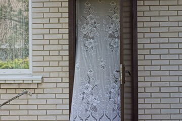 Poster - one open brown metal door with a white curtain on a gray brick wall with a window on the street