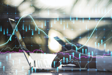 Fototapete - Close up of hands using laptop and smartphone at desktop with abstract glowing forex graph on blurry outdoor background with candlestick. Invest, trade and broker concept. Double exposure.