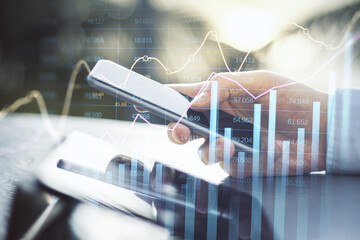 Poster - businessman hand using smartphone and tablet at desktop with abstract glowing business chart with index and growth on blurry background. Finance, trade and market report concept. Double exposure.