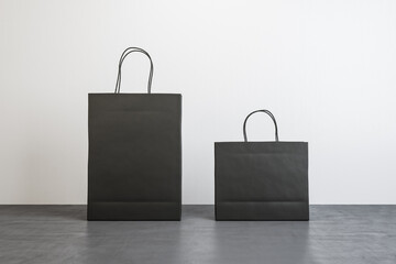 Front view on two black blank paper shopping bags with place for your logo or text on concrete floor on white background. 3D rendering, mockup