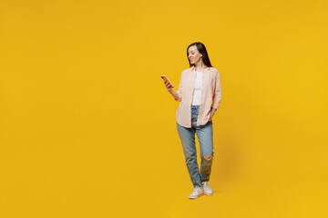 Wall Mural - Full body young happy smiling cheerful woman she 30s wears striped shirt white t-shirt hold in hand use mobile cell phone isolated on plain yellow background studio portrait. People lifestyle concept.