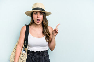 Young caucasian woman holding beach bag isolated on blue background pointing to the side