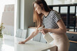 Portrait of beautiful young woman cleaning white table with spray and cloth on modern kitchen side view. Housekeeper tidy up kitchen furniture with cleanser. Clean and beautiful home