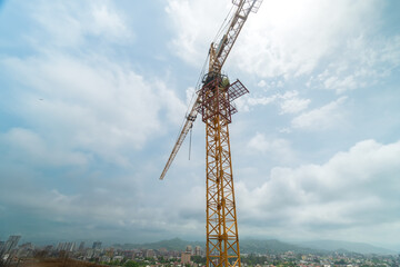 Wall Mural - Close-up of a construction crane on a construction site with protruding fittings for screed against the background of mountains and cloudy sky
